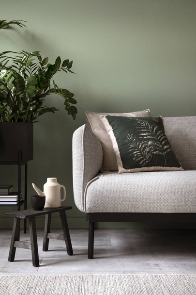 Κομψή σύνθεση του εσωτερικού του σαλονιού. Μοντέρνος καναπές, σχεδιαστικά μαξιλάρια, φυτά σε μεταλλική κατσαρόλα και δημιουργικά προσωπικά αξεσουάρ. Ευκάλυπτος πράσινος τοίχος. Πρότυπο. Αντιγραφή χώρου.  - Φωτογραφία, εικόνα