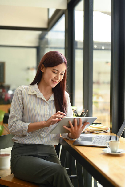 Attractive female freelancer checking online information or email on her digital tablet. - Fotó, kép
