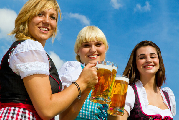 Tres chicas en dirndl colorido beber cerveza en un campo - Foto, imagen