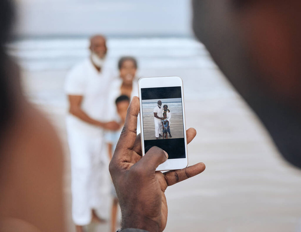 Cropped shot of an unrecognizable man taking a picture of a mature couple and their grandson at the beach. - Foto, afbeelding