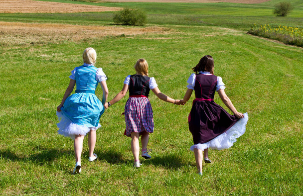 Drie meisjes in kleurrijke dirndl lopen op een weide - Foto, afbeelding