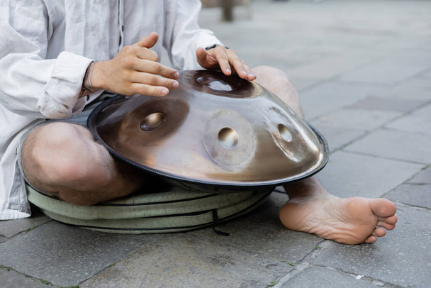 Cropped view of barefoot man playing hang drum on urban street  - 写真・画像