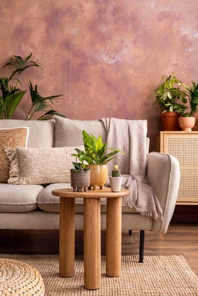 Stylish composition of creative spacious living room interior with plants, sofa, coffee table, rattan chest of drawers and stylish accessories. Botanical space of a cozy room. Brown walls. Template.  - Photo, Image