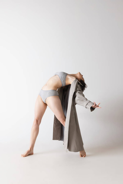 Feelings. Dynamic portrait of young flexible woman in lingerie and coat dancing isolated on grey background. Art, motion, action, flexibility, inspiration concept. Solo performance - Фото, изображение