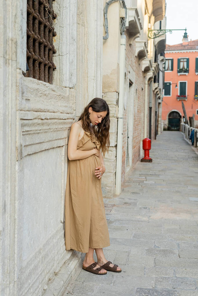 Young pregnant woman in dress touching belly on urban street in Italy  - 写真・画像