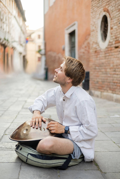 Side view of smiling musician playing handpan on urban street in Venice  - Foto, Imagen