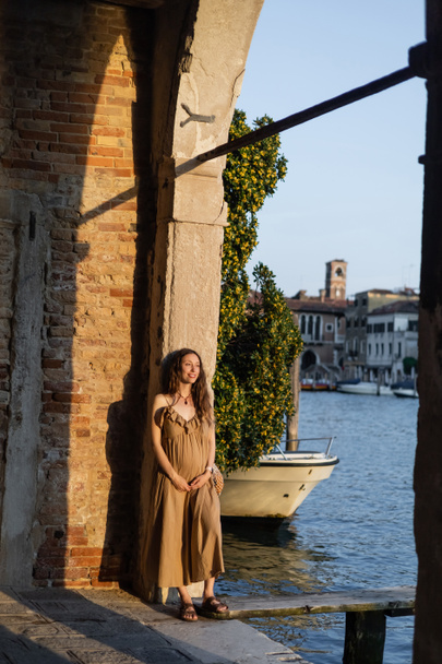Cheerful pregnant woman standing in arch near pier in Venice  - Fotografie, Obrázek