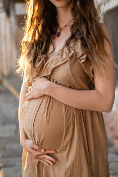Rajatut näkymä raskaana oleva nainen koskettaa vatsa seisoessaan auringonvalossa kaupunkien kadulla  - Valokuva, kuva
