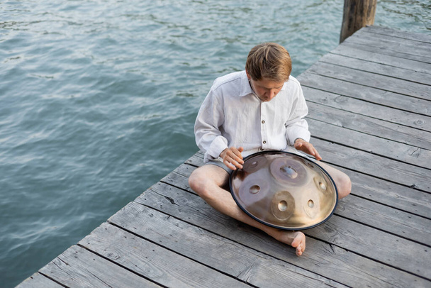 Overhead view of man playing hang drum on wooden pier above river in Venice  - Photo, Image