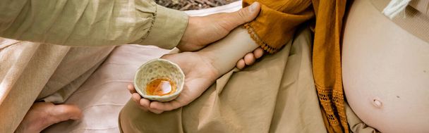 Vista recortada del hombre tocando esposa embarazada durante la ceremonia del té en el bosque, pancarta  - Foto, Imagen