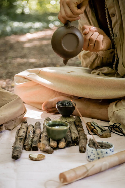 Vágott kilátás az ember öntő tea tálban közelében vargan a takaró az erdőben  - Fotó, kép