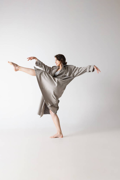 Contemp. Dancing young thin woman in lingerie and coat in motion isolated on grey background. Art, motion, action, flexibility, inspiration concept. Copy space for ad, design - Foto, imagen