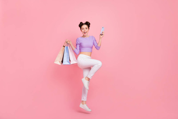Full length body size view of pretty trendy girl jumping using device buy clothes wear isolated over pink pastel color background. - Photo, Image