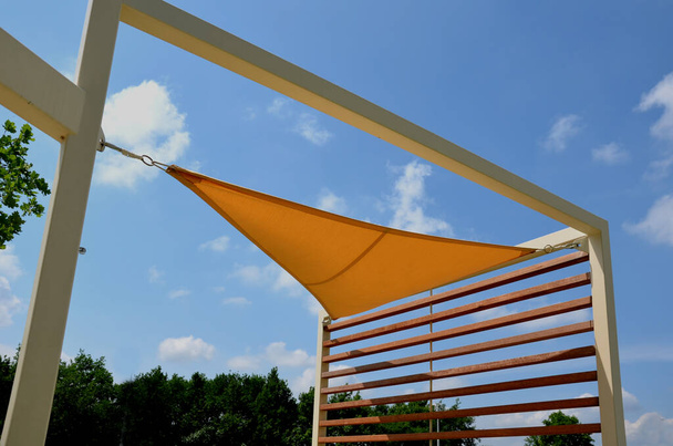 yellow canvas stretched, shading from the sun and rain over the terrace of the restaurant, on the playground in the kindergarten, on promenade. pergola with wooden gray beams, on white metal steel - 写真・画像