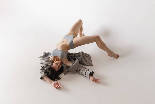 Feelings. Aerial view of young sensual woman in lingerie and coat dancing isolated on grey background. Art, motion, action, flexibility, inspiration concept. Solo performance - Фото, изображение