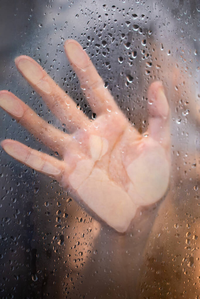 Weibliche Hand und unkenntliche Silhouette hinter nassem Glas in der Dusche - Foto, Bild