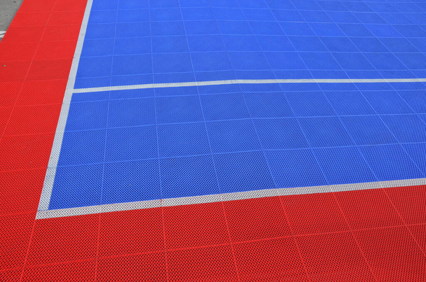Una cancha de voleibol fue creada en el estacionamiento. las baldosas conectadas y portátiles forman una plataforma de plástico rojo-azul en el suelo de hormigón. colchón, rejilla plástica, caucho, suave - Foto, imagen