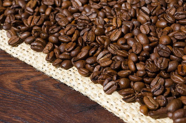 Roasted coffee beans on burlap on a wooden table, close-up. Arabica is the most common type of coffee. - Photo, Image