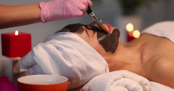 Cosmetologist applied black alginate mask to skin on patient face. Rejuvenation and facial skin care concept - Metraje, vídeo