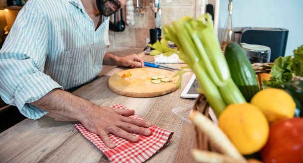Ein unkenntlich gemachter männlicher Koch putzt die hölzerne Küchentheke mit kariertem roten Geschirrtuch. Bild ausschneiden, Nahaufnahme - Foto, Bild