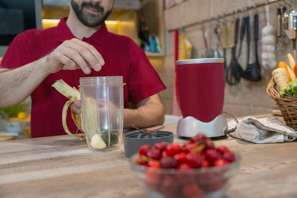 Man preparing healthy smoothie for diet raw vegetarian breakfast. Mature male in the kitchen making fresh nutrition drink from fresh vegetables - Photo, image