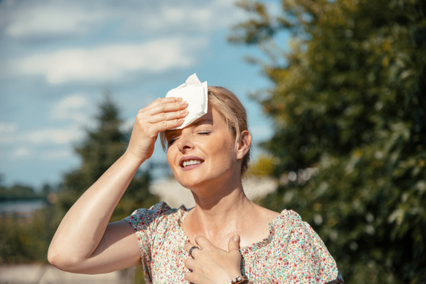 Woman feeling bad pain, heat, woman with heatstroke. Having sunstroke at summer hot weather. Mature Female under sunshine suffering from Headache. Person holds paper tissue on head - Photo, Image
