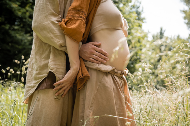 Cropped view of man hugging pregnant woman in field  - Fotografie, Obrázek