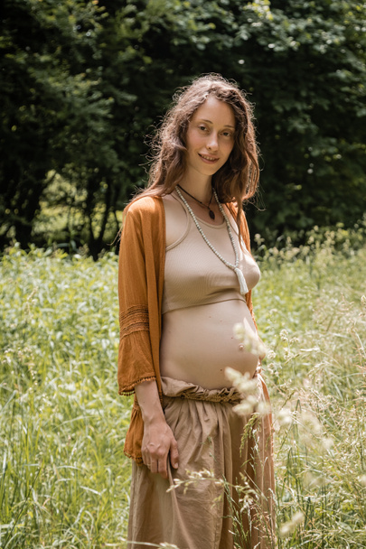 Портрет усміхненої вагітної жінки, яка дивиться на камеру в полі
  - Фото, зображення