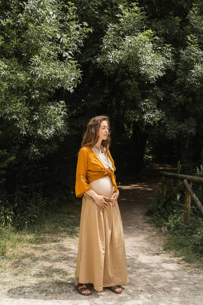 Pregnant woman standing on walkway in summer forest  - Fotografie, Obrázek