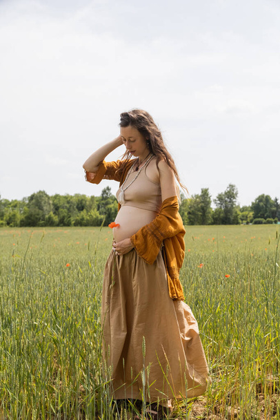 Pregnant woman holding pappy flower while standing in field  - Foto, immagini
