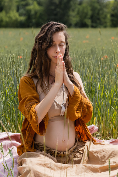 Young pregnant woman praying on blanket in field  - Zdjęcie, obraz