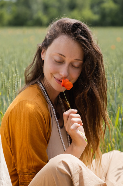 Usmívající se mladá žena čichající mák květ v poli  - Fotografie, Obrázek