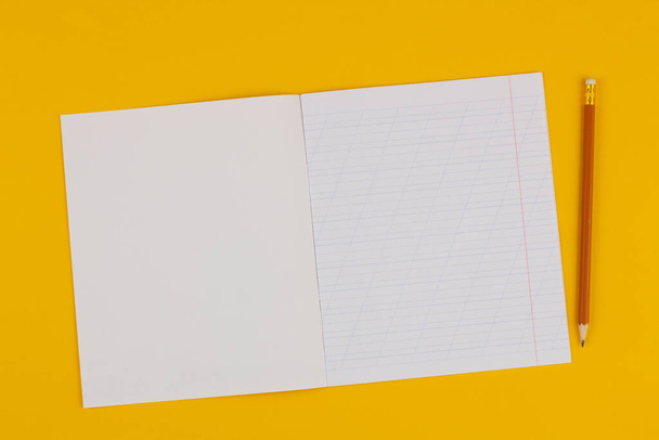 Шкільний блокнот на жовтому тлі з копіювальним простором для тексту та олівця. Повернутися до школи. Порожній аркуш паперу з косими лініями в тренувальній книзі. шкільне приладдя. Вид зверху
 - Фото, зображення