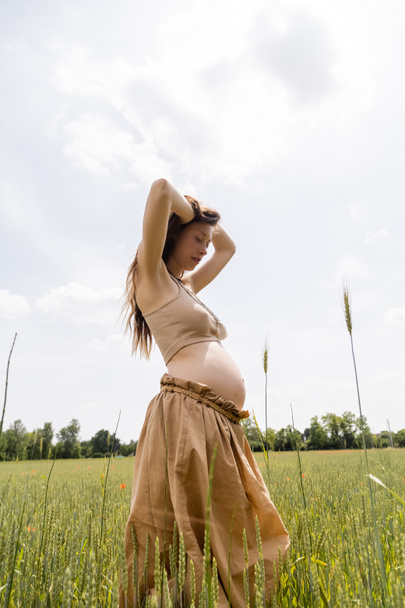 Low angle view of pregnant woman standing in summer field  - Foto, Bild