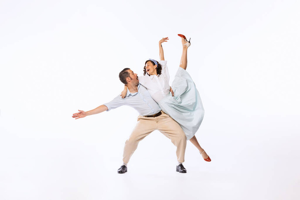 Portrait of young emotive couple, man and woman, dancing retro dance isolated over white studio background. Concept of vintage fashion, hobby, activity, art, music, party, creativity and ad - Fotó, kép