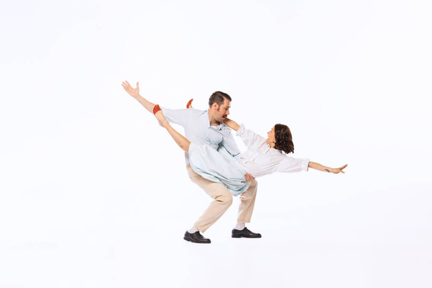 Portrait of young beautiful couple, man and woman, dancing twist isolated over white studio background. Concept of vintage fashion, hobby, activity, art, music, party, creativity and ad - Photo, Image