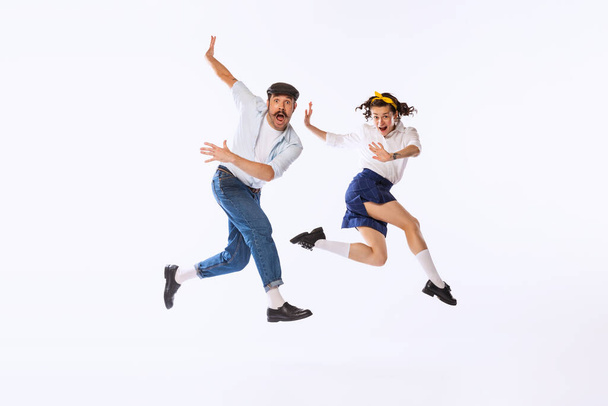 Portrait of beautiful emotive couple, man and woman, dancing, posing in a jump isolated over white studio background. Concept of vintage fashion, hobby, activity, art, music, party, creativity and ad - Photo, image