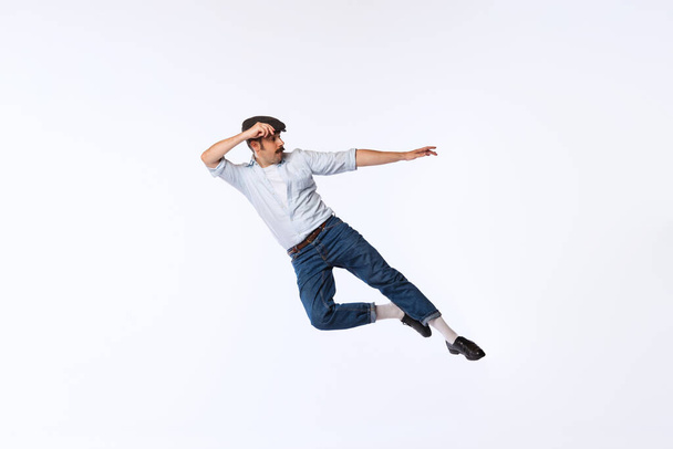 Portrait of stylish young man in retro outfit dancing, posing isolated over white studio background. Concept of vintage fashion, hobby, activity, art, music, party, creativity and ad - Zdjęcie, obraz