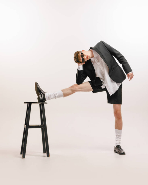 Eccentric. One young stylish man, student in black shorts and jacket posing isolated over white background. Modern business style clothes. Concept of art, beauty, fashion, youth culture, sales and ads - Foto, Imagem