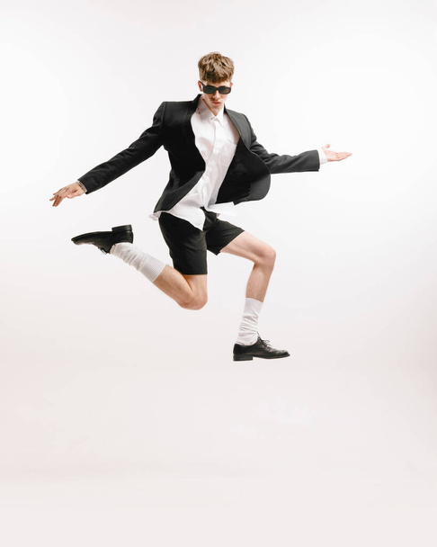 Fun. Young astonished man in black shorts and jacket jumping isolated over white background. Modern business style clothes. Concept of art, beauty, fashion, youth culture, sales and ads - Фото, зображення