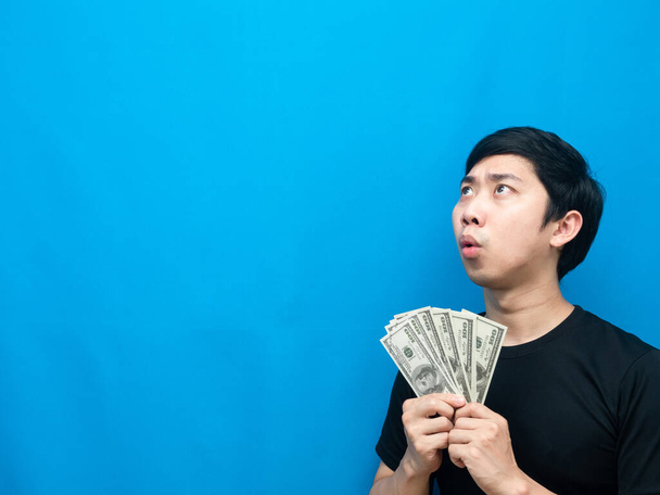 Man holding money feeling amazed looking at copy space blue background - Foto, Imagen