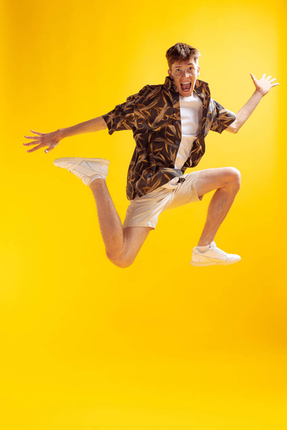 Delight. Full-length mans portrait isolated on bright yellow studio backgroud. Young emotional man jumping. Human emotions, facial expression concept. Summer fachion collection - Фото, изображение