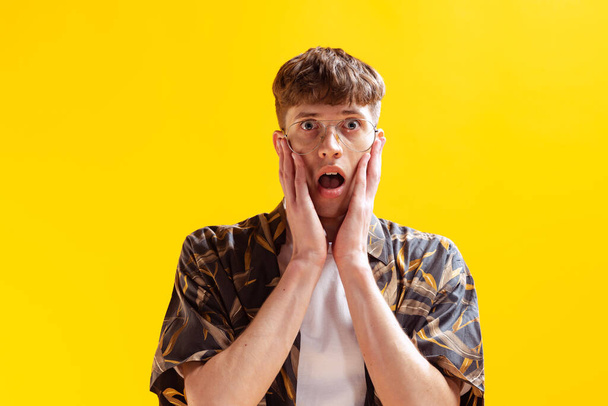 Wow, shock. Closeup portrait of handsome young man, teen looking at camera isolated on bright yellow studio backgroud. Human emotions, facial expression, summer fashion collection concept. - Photo, image