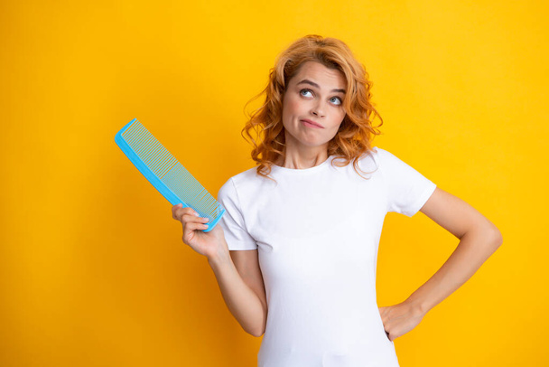 Surprised amazed girl combing hair. Redhead woman with a comb, isolated on yellow background. Women hair care - Photo, image
