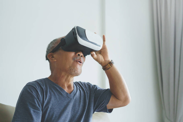 Excited Asian Senior man wearing VR goggles and enjoying playing video games with virtual reality headset - 写真・画像
