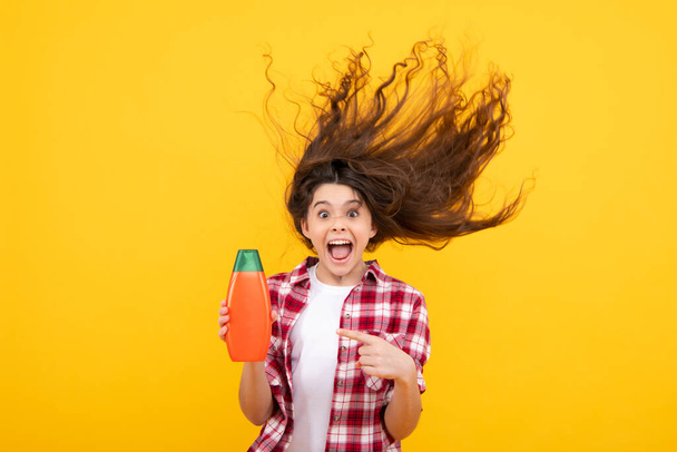 Εκπληκτική έφηβη. Teenager κορίτσι παιδί δείχνει μπουκάλι σαμπουάν conditioners ή αφρόλουτρο. καλλυντικό προϊόν μαλλιών. Μπουκάλι για διαφήμιση mock up αντίγραφο χώρου. Ενθουσιασμένη έφηβη - Φωτογραφία, εικόνα