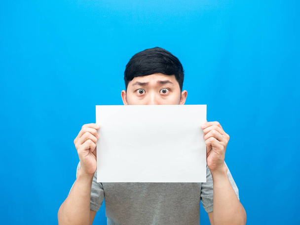 Man holding empty sheet close his face on blue background - Photo, Image