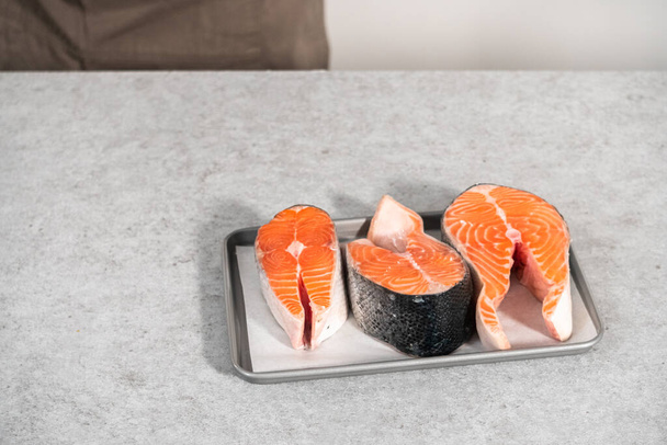 Farm-raised salmon steaks on a cooking tray with a parchment paper. - Fotó, kép