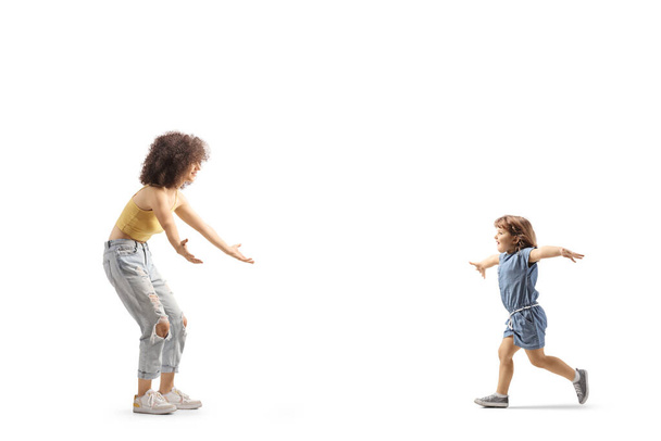 Full length profile shot of a little girl runnuning towards a young female with curly afro hairstyle isolated on white background - Valokuva, kuva