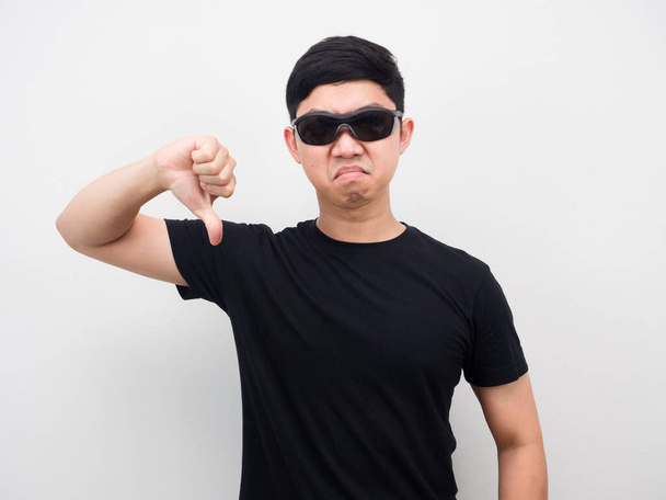 Homme portant des lunettes de soleil visage en colère montrer pouce vers le bas fond blanc - Photo, image